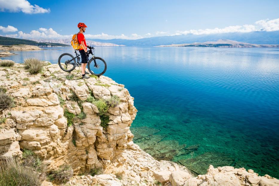 Ein Radfahrer steht mit seinem Mountainbike auf einer Klippe mit Blick auf das Meer.
