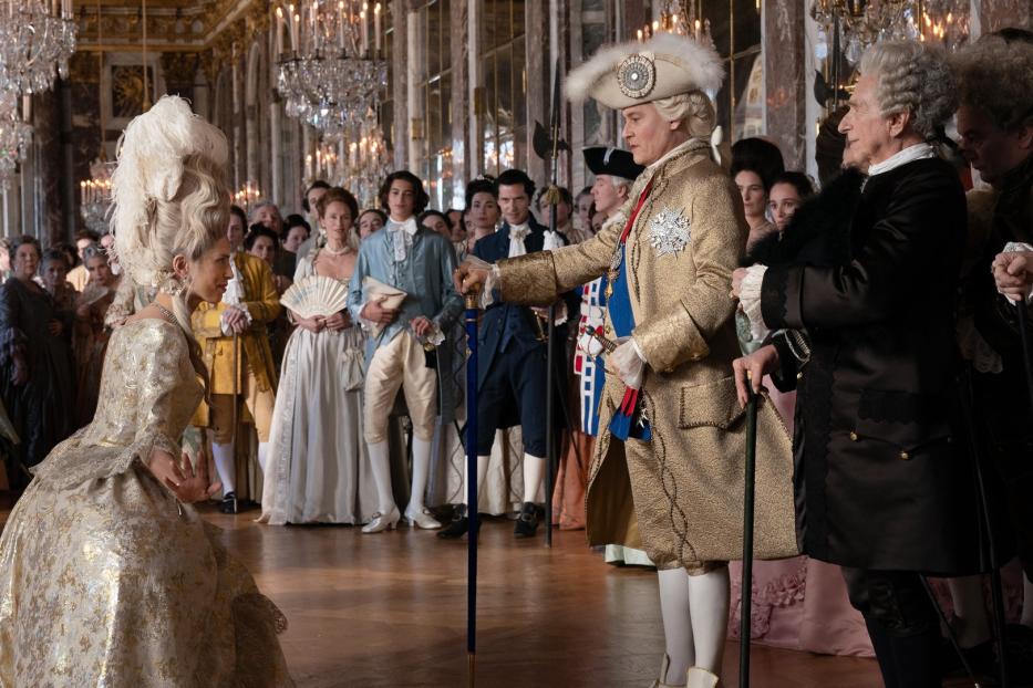 Szene in einem opulenten Ballsaal mit kostümierten Personen im Stil des 18. Jahrhunderts.