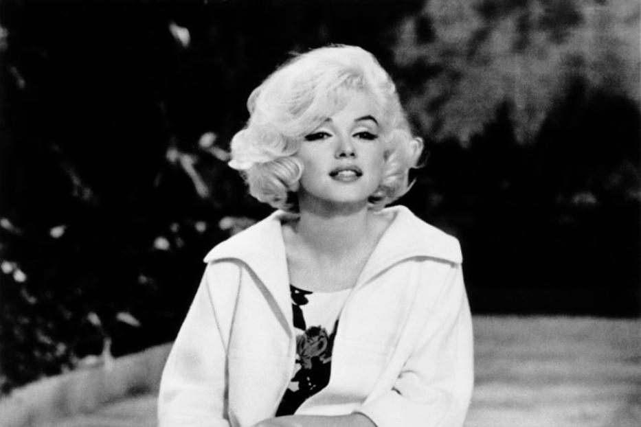 Marilyn Monroe hockt in einem weißen Kleid und Blazer.