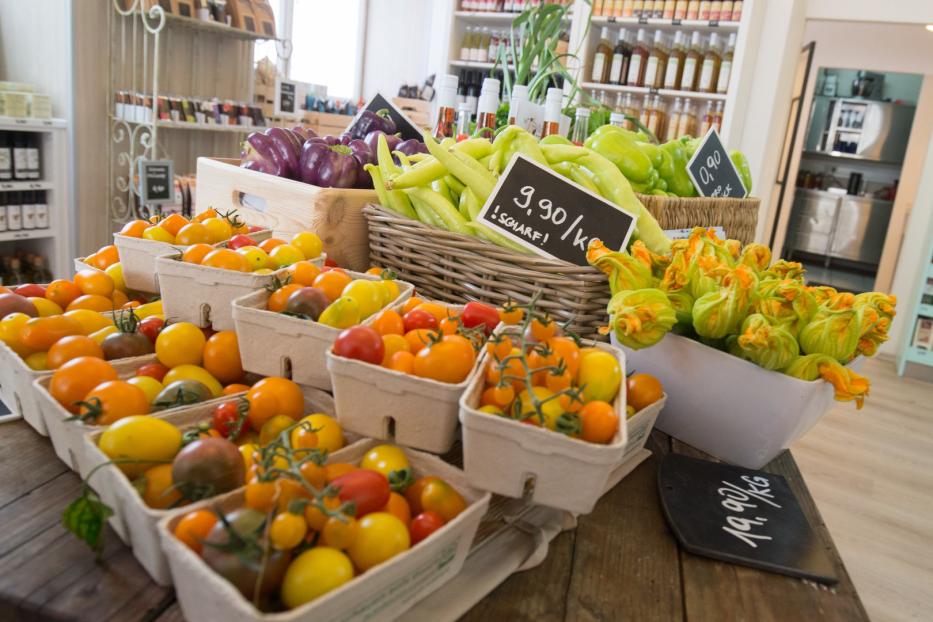 Verschiedene Gemüsesorten, darunter Tomaten, Paprika und Zucchiniblüten, werden in einem Laden zum Verkauf angeboten.