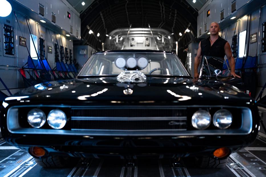 Vin Diesel posiert mit einem schwarzen Dodge Charger in einem Flugzeug.