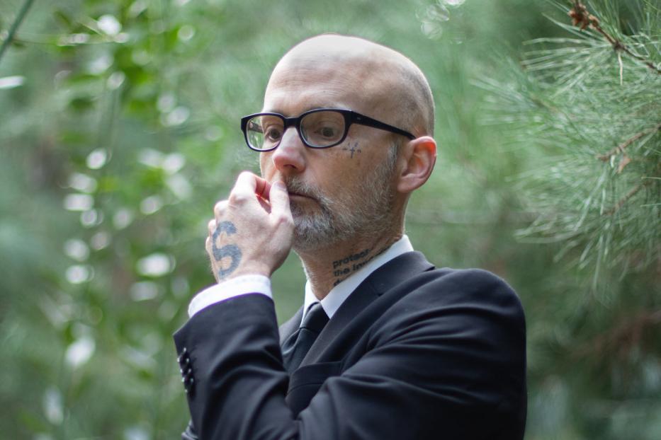 Moby in einem schwarzen Anzug steht nachdenklich im Grünen.