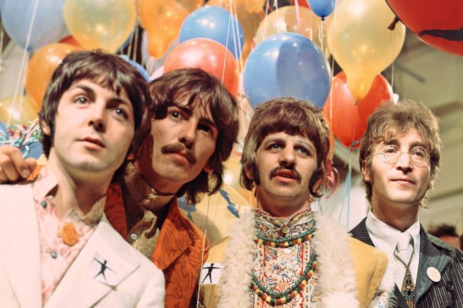 Die Beatles stehen vor einem Hintergrund aus bunten Luftballons.