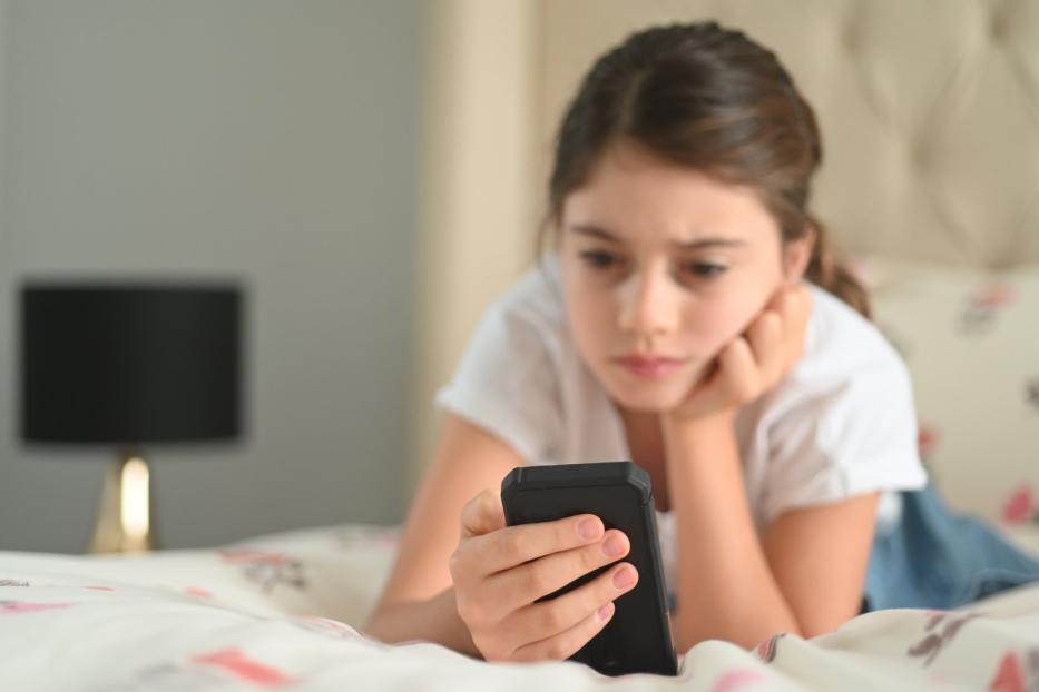 Ein Kind liegt mit einem Smartphone auf dem Bett.