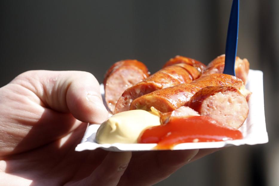 Eine Hand hält eine Schale mit geschnittener Bratwurst, Senf und Ketchup.