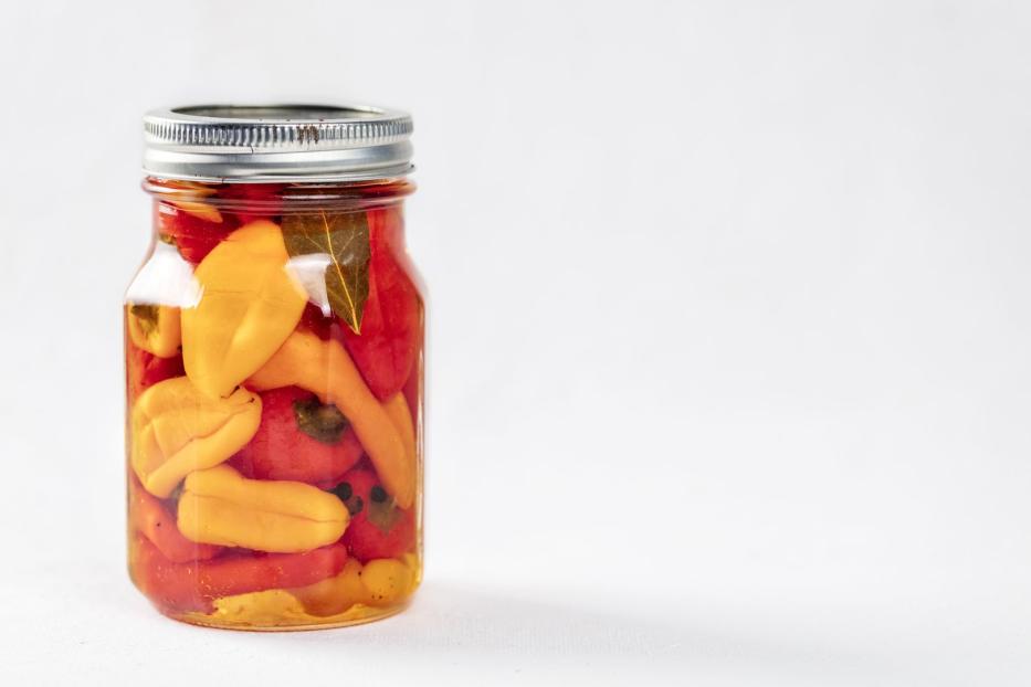Einmachglas mit eingelegten gelben und roten Paprika auf weißem Grund.
