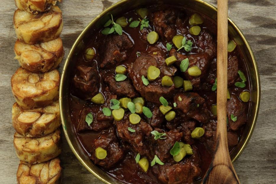 Rindsgulasch mit Gurken und Semmelknödel auf einem Holztisch.