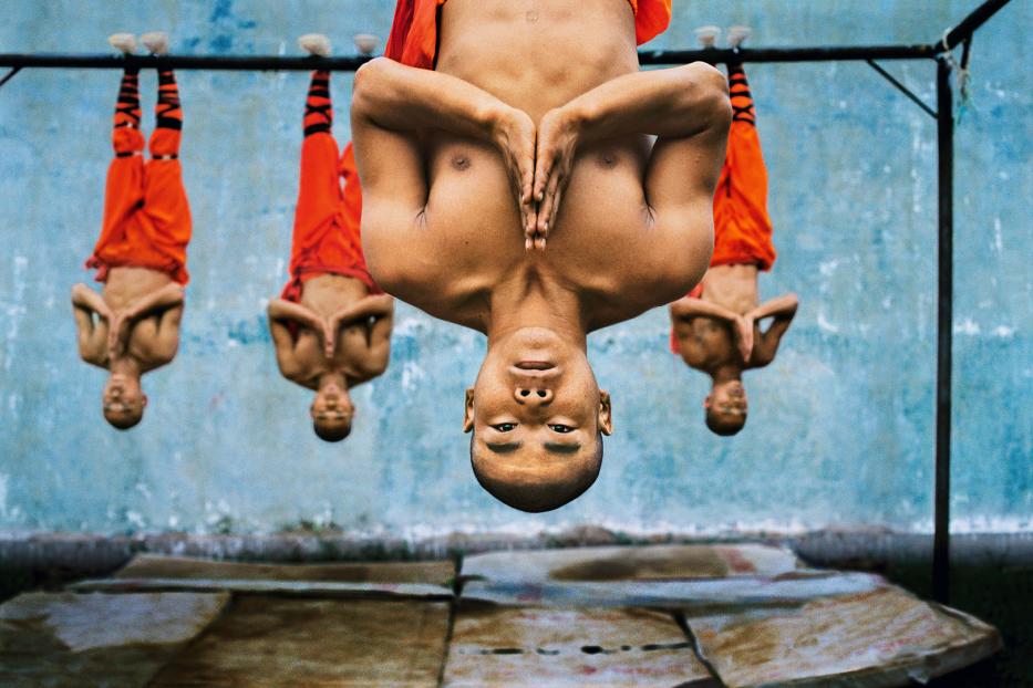 Shaolin Mönche hängen kopfüber an einer Stange.