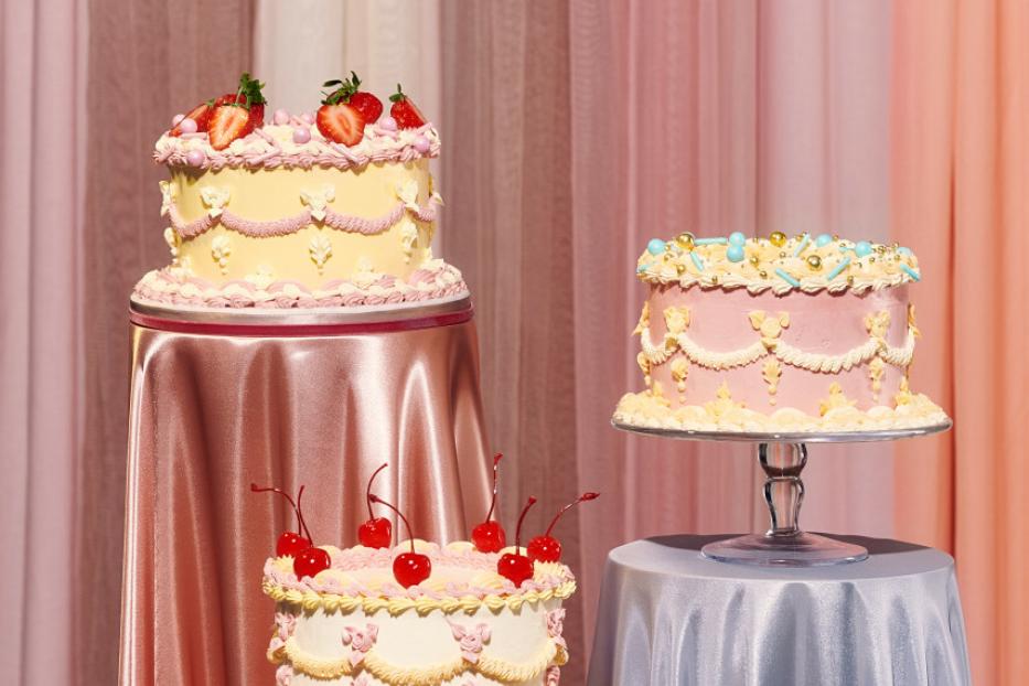 Drei verzierte Kuchen stehen auf Tischen mit pastellfarbenen Tischdecken.