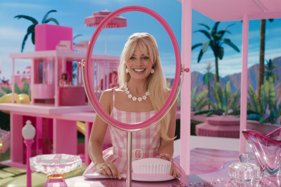 Margot Robbie als Barbie vor ihrem pinkfarbenen Haus mit Pool und Palmen.