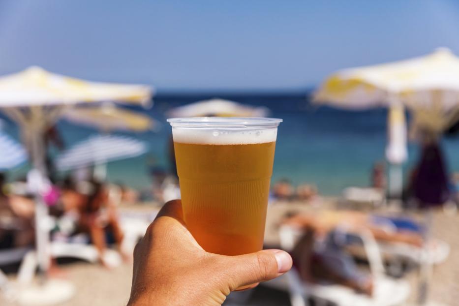 Ein Mann hält ein Bier am Strand in der Hand.