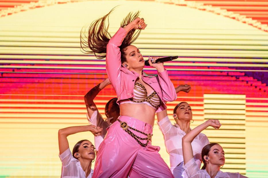 Rosalía tritt in einem pinkfarbenen Outfit mit Tänzern auf einer Bühne auf.