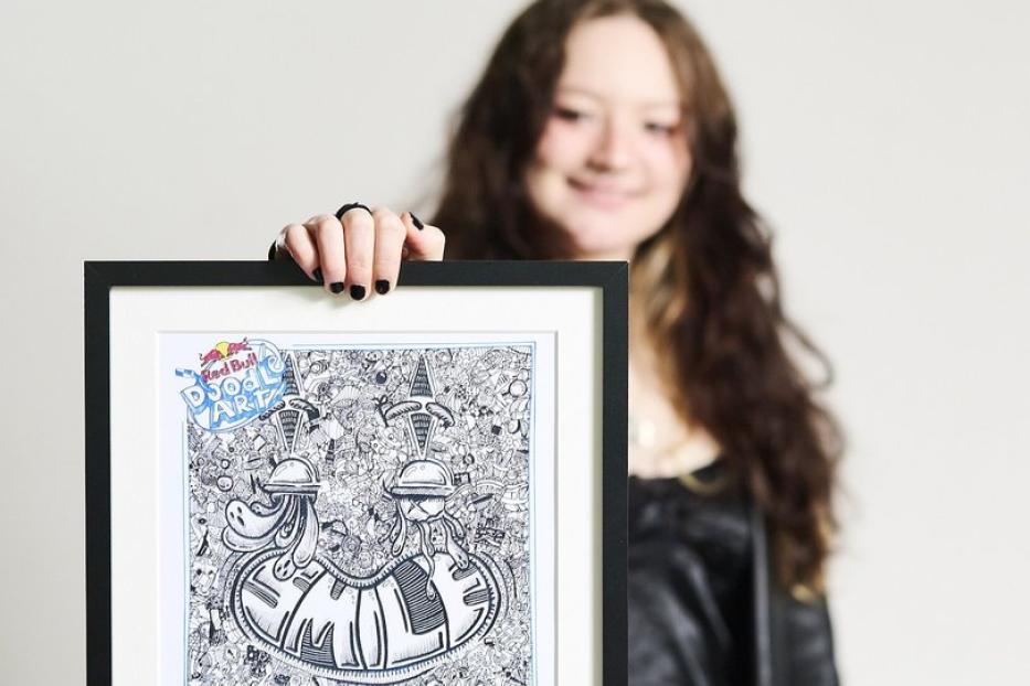 Eine junge Frau präsentiert ein gerahmtes Doodle-Art-Bild von Red Bull.