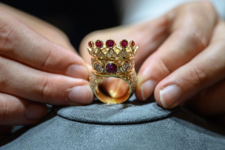 Ein goldener Ring in Form einer Krone mit Rubinen wird von Händen gehalten.