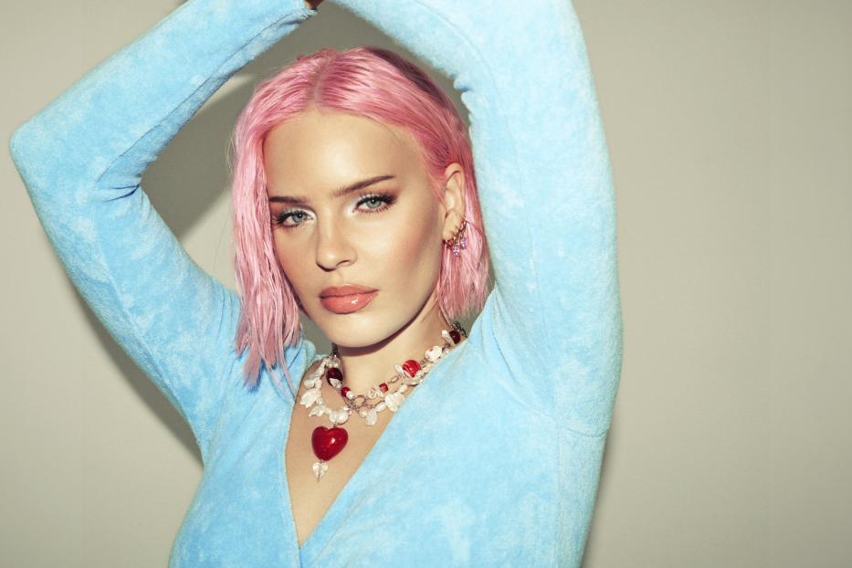 Anne-Marie posiert mit pinken Haaren und blauem Oberteil für ein Foto.