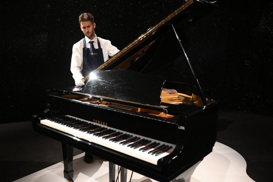 Ein Mann mit Schürze steht an einem schwarzen Yamaha-Flügel.
