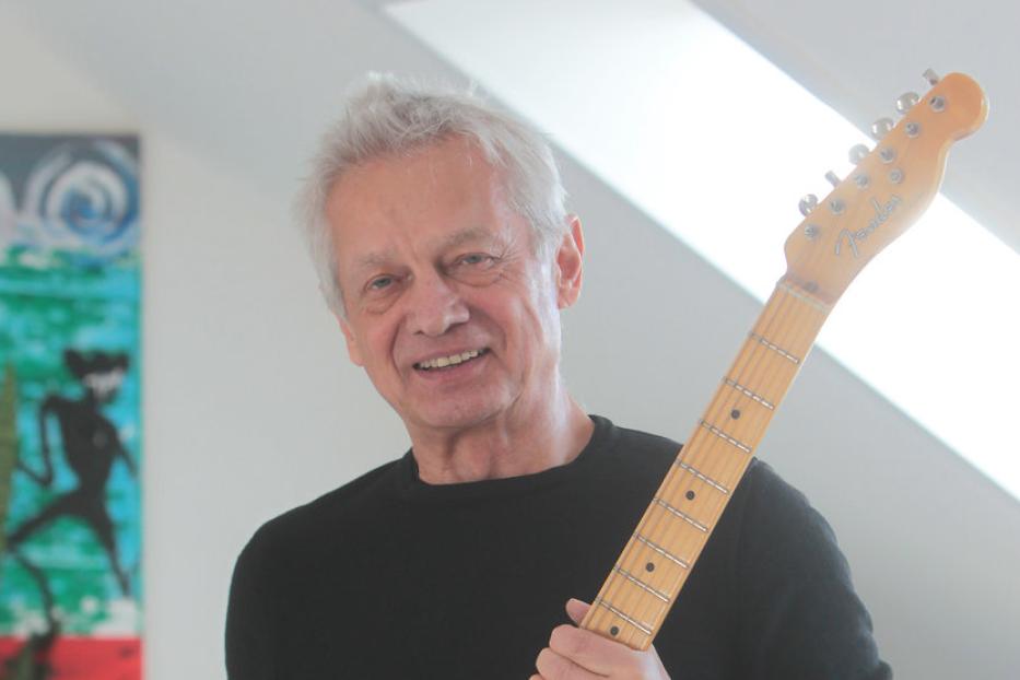 Ein lächelnder Mann mittleren Alters hält eine E-Gitarre der Marke Fender.
