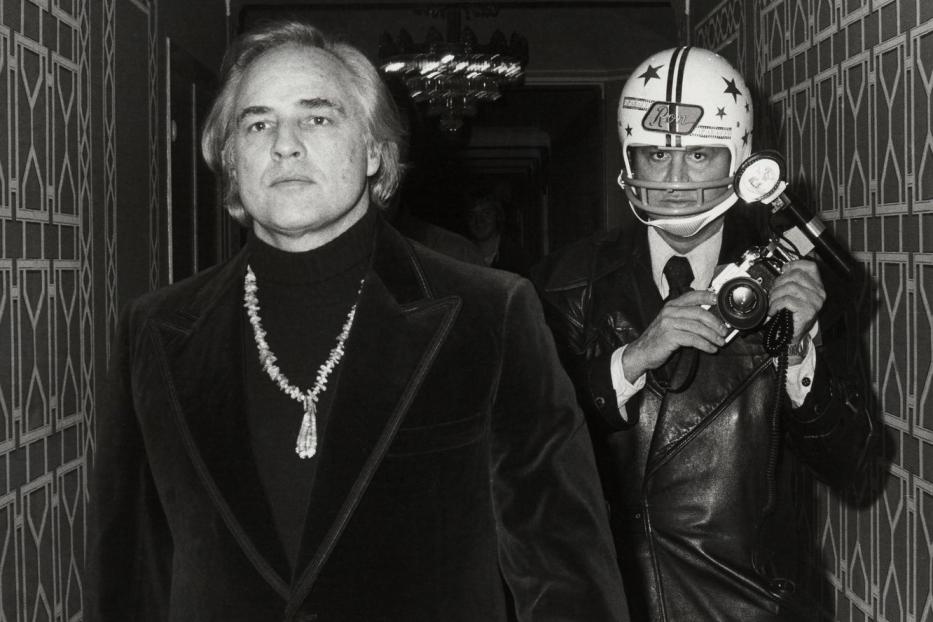 Marlon Brando und ein Fotograf mit Footballhelm stehen in einem Flur.