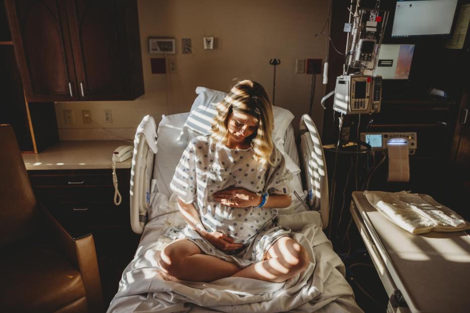 Eine schwangere Frau berührt ihren Bauch, während sie in einem Krankenhausbett sitzt.