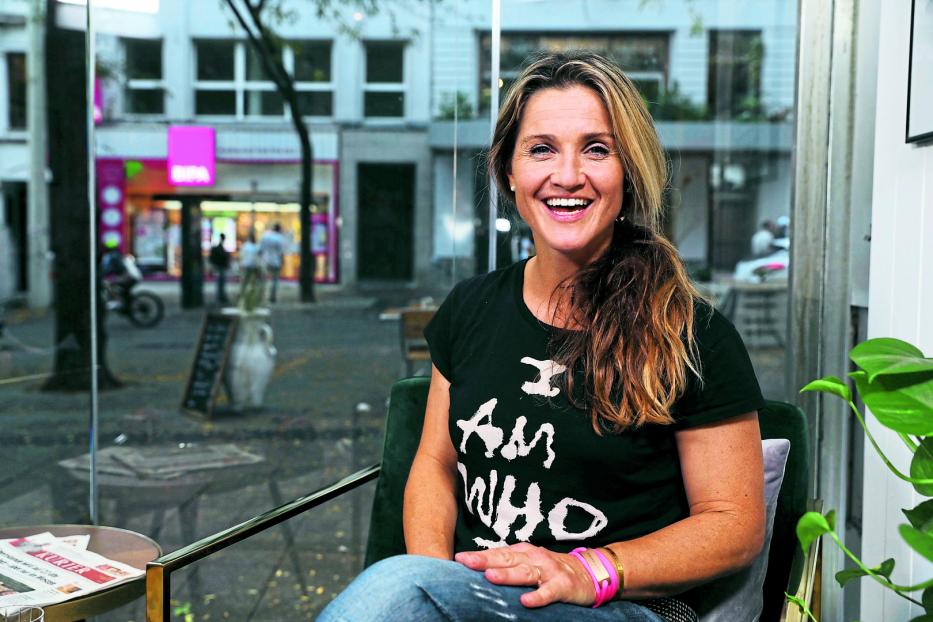 Eine lächelnde Frau sitzt in einem Café mit Blick auf die Straße.
