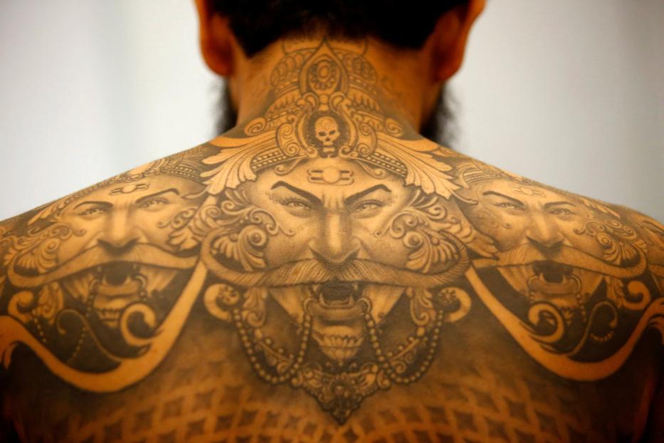 Ein Mann mit einem detaillierten Tattoo von drei Gesichtern auf seinem Rücken.