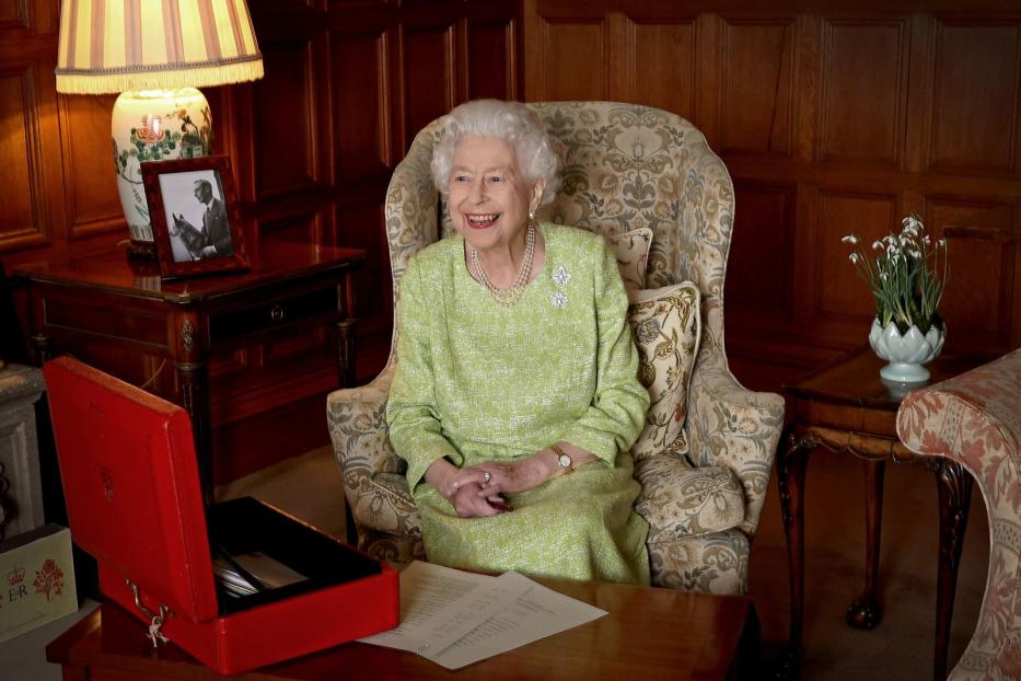 Königin Elizabeth II. sitzt lächelnd in einem Sessel in einem Wohnzimmer.