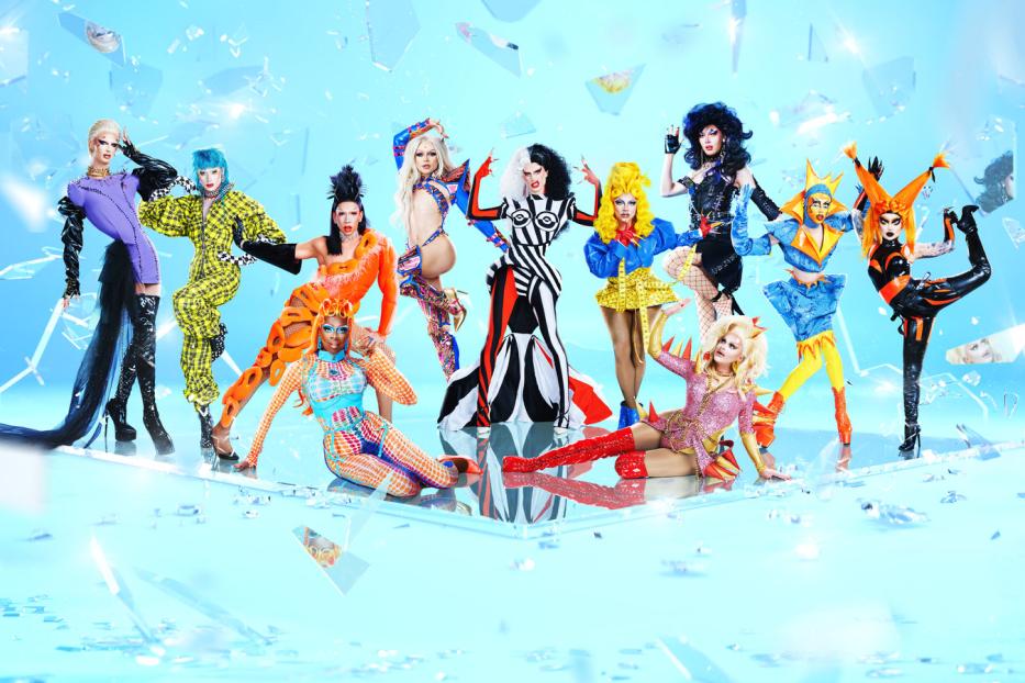 Eine Gruppe von Drag Queens posiert vor einem hellblauen Hintergrund mit Glasscherben.