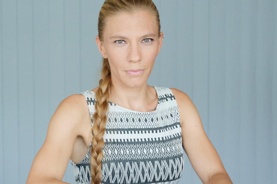 Eine Frau mit blonden Haaren und einem gemusterten Kleid sitzt an einem Tisch.