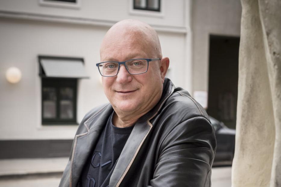 Ein Mann mit Brille und Lederjacke lehnt an einem steinernen Geländer.