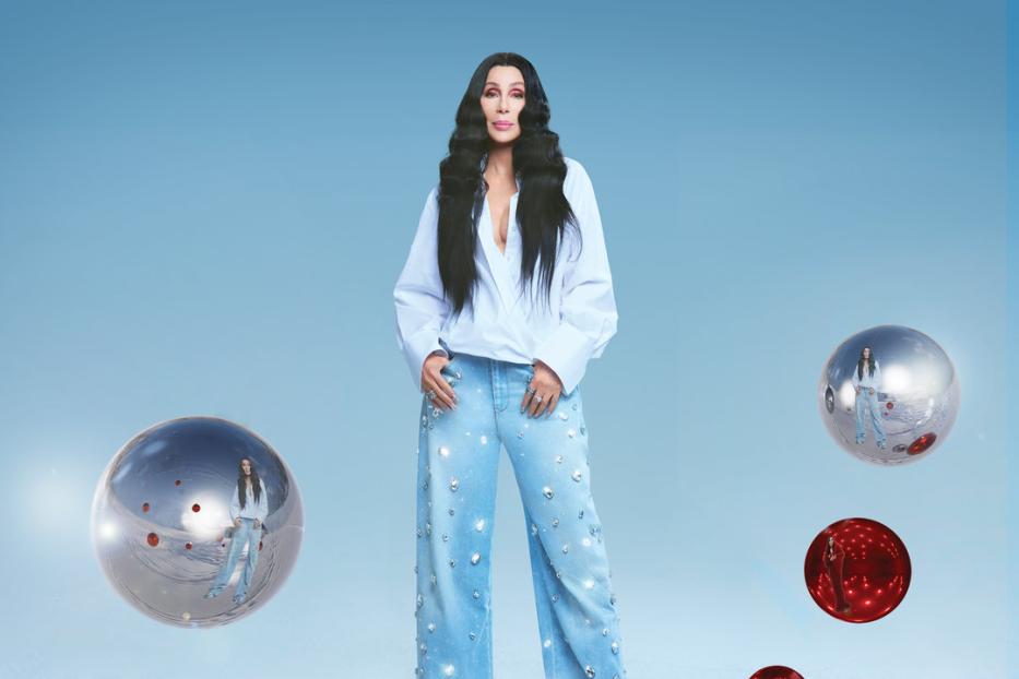 Cher steht auf einer schneebedeckten Oberfläche, umgeben von roten und silbernen Kugeln.