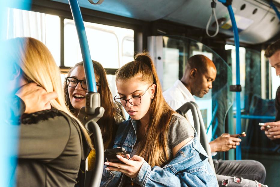 Mehrere Personen fahren mit einem Bus und benutzen ihre Smartphones.