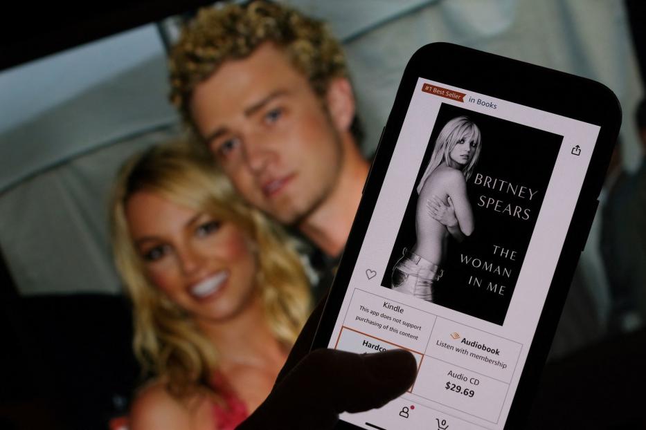 Ein Smartphone zeigt das Buch „The Woman in Me“ von Britney Spears; im Hintergrund ein Foto von ihr und Justin Timberlake.