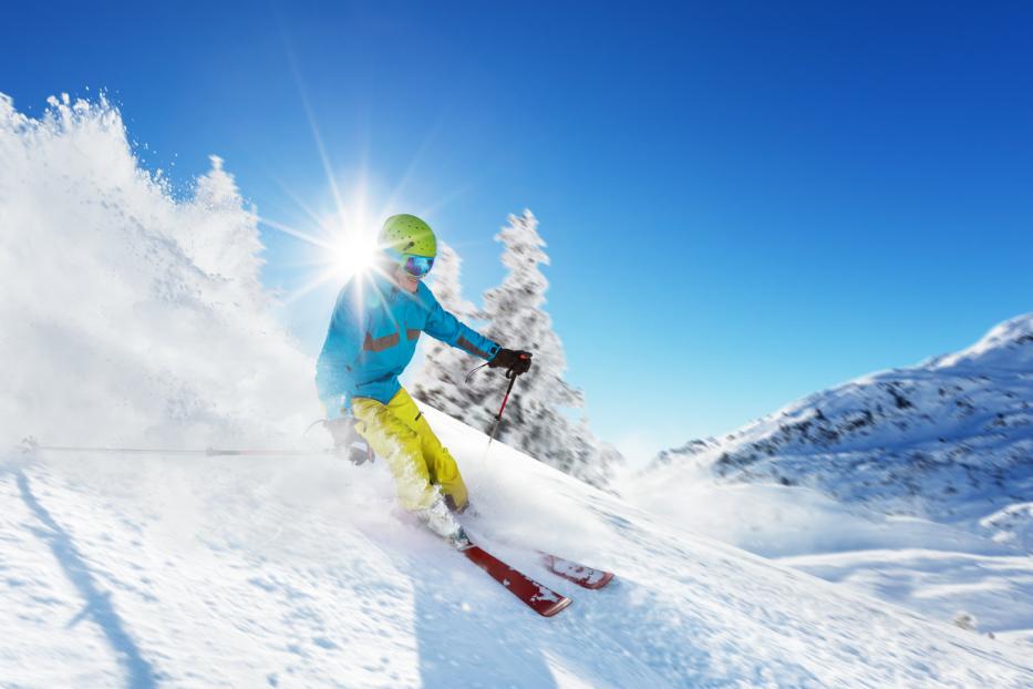 Ein Skifahrer fährt an einem sonnigen Tag eine schneebedeckte Piste hinunter.