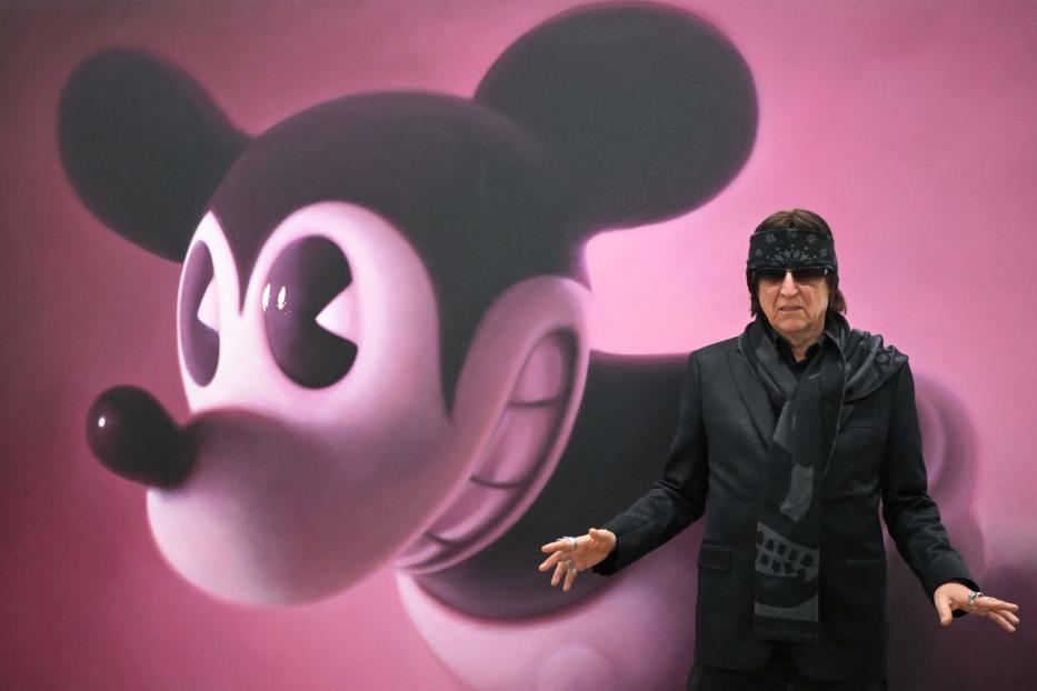 Ein Mann mit Sonnenbrille und Kopftuch posiert vor einem großen Mickey-Mouse-Gemälde.