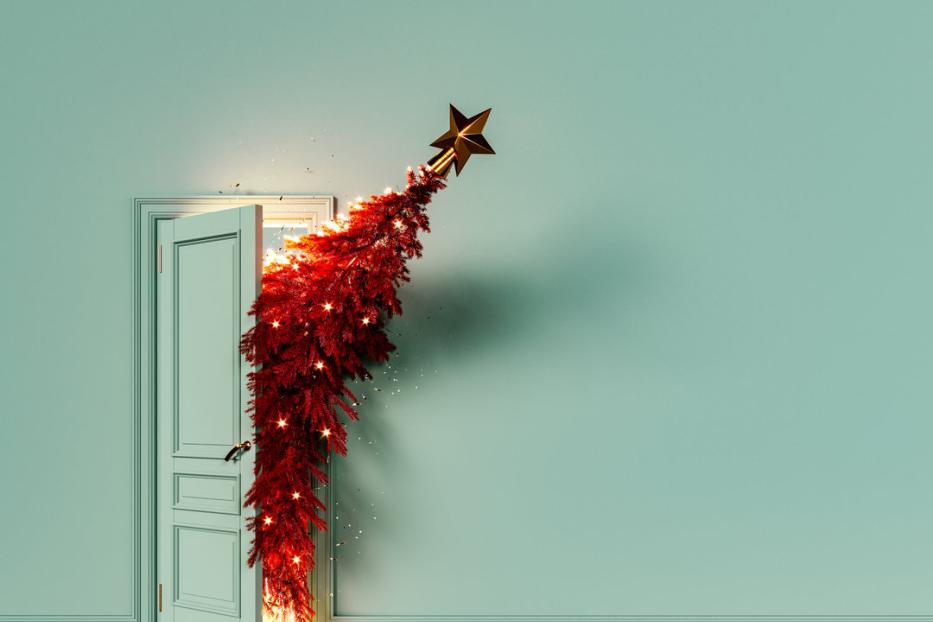 Ein rot geschmückter Weihnachtsbaum scheint aus einer offenen Tür in einem mintgrünen Raum zu wachsen.