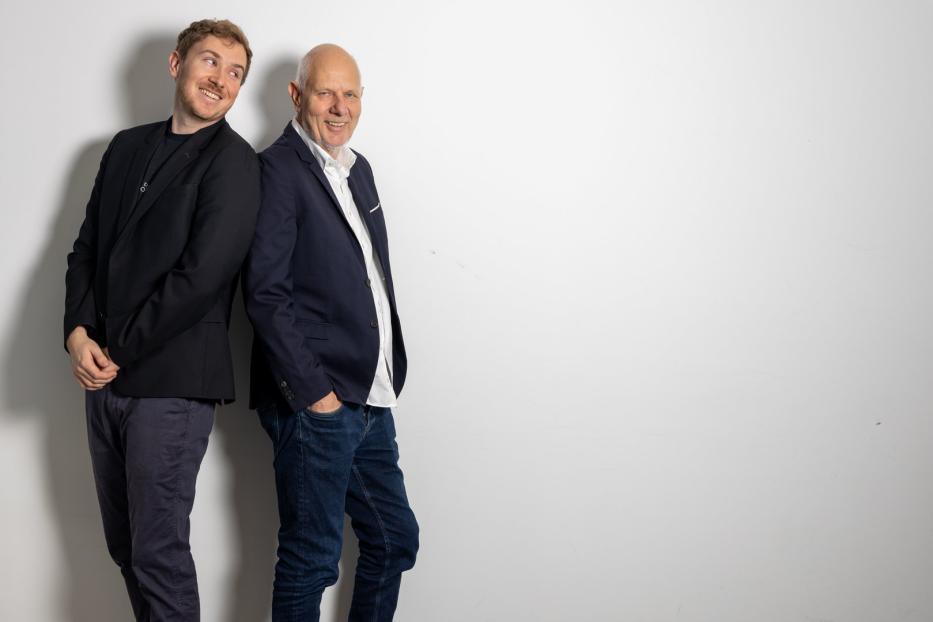 Matthias und Tristan Horx stehen Rücken an Rücken vor einer weißen Wand.