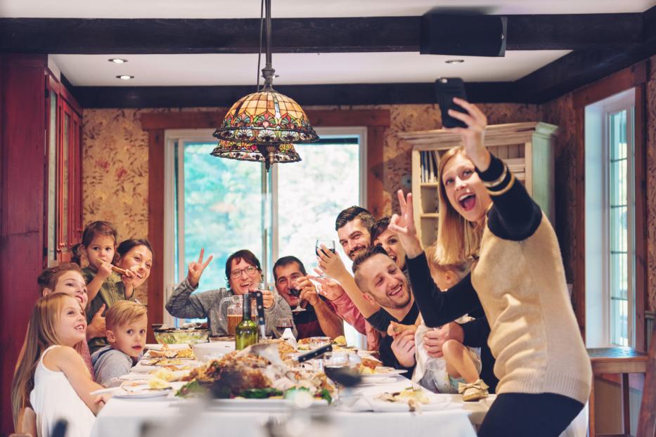 Eine Familie sitzt an einem Tisch mit Essen und macht ein Selfie.