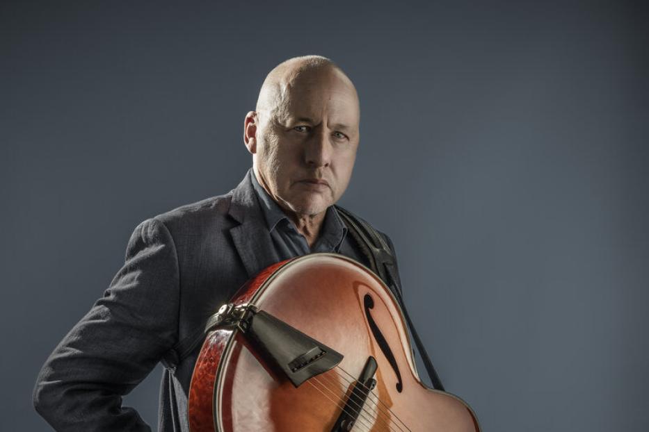 Ein Mann im Anzug hält eine Archtop-Gitarre.