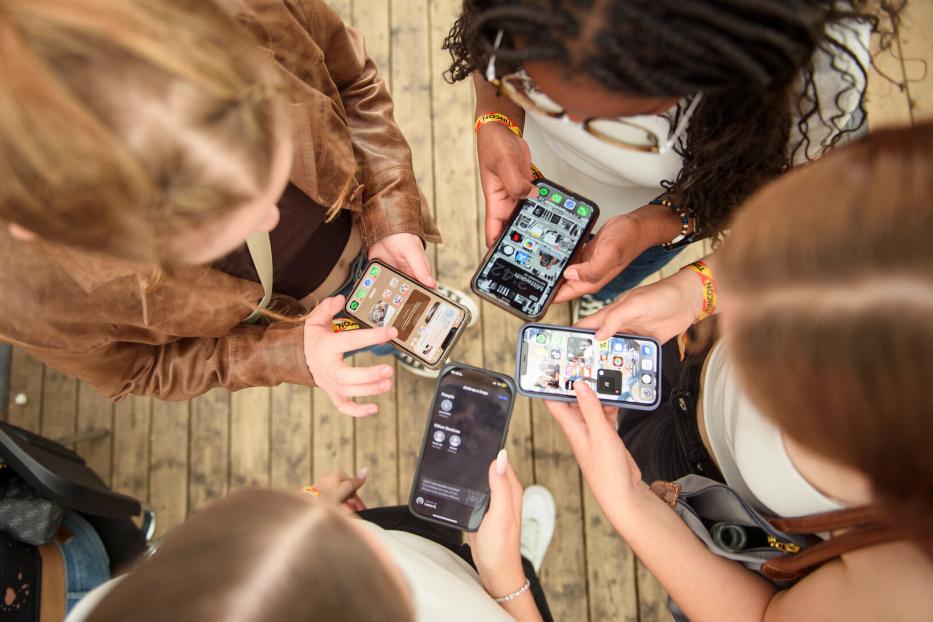 Fünf junge Frauen stehen im Kreis und schauen auf ihre Smartphones.