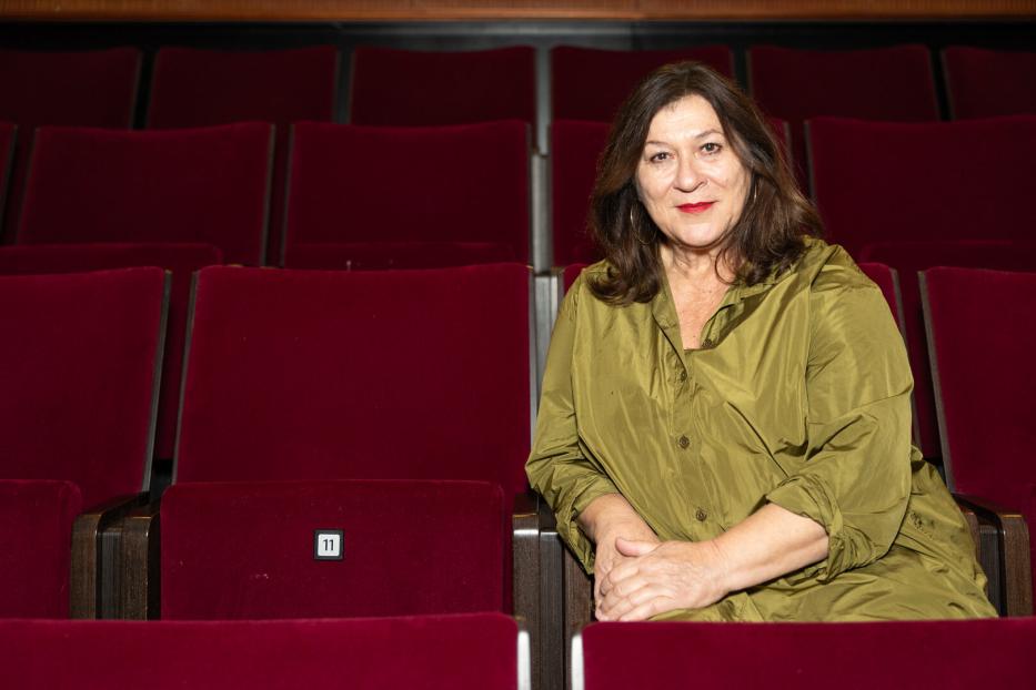 Eine Frau sitzt in einem leeren Theatersaal mit roten Sitzen.