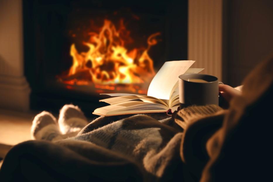 Eine Person liest ein Buch und trinkt eine Tasse Kaffee vor einem Kamin.