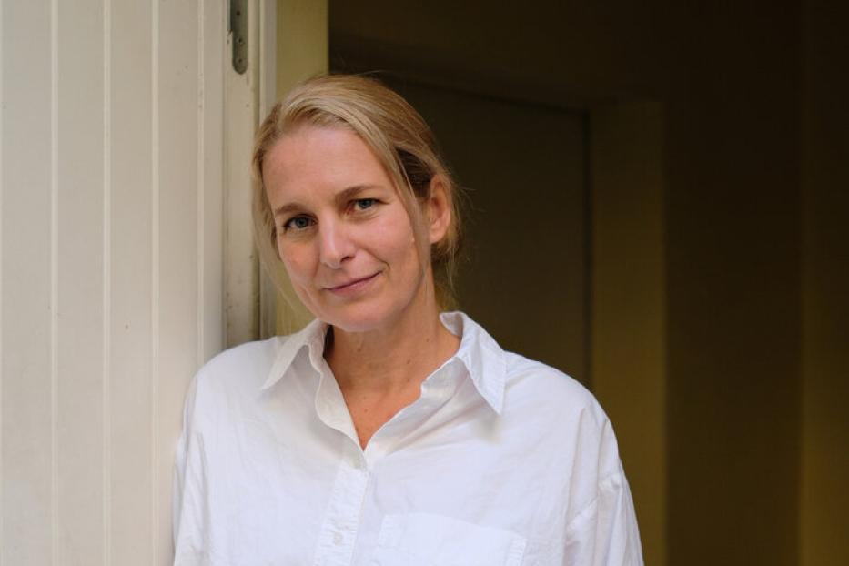 Eine Frau mit blonden Haaren lehnt an einer Tür.