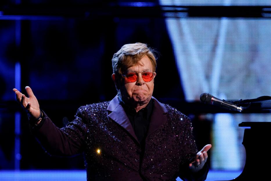 Elton John mit roter Brille und glitzerndem Sakko gestikuliert am Klavier.