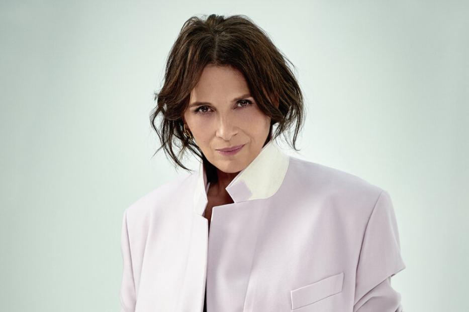 Porträt von Juliette Binoche in einem helllila Hosenanzug.