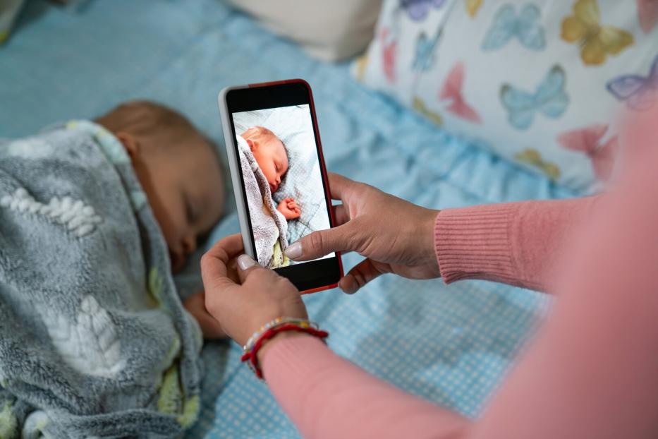 Eine Person fotografiert mit einem Smartphone ein schlafendes Baby.