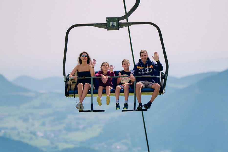 Eine Familie fährt gemeinsam in einem Sessellift über eine Berglandschaft.