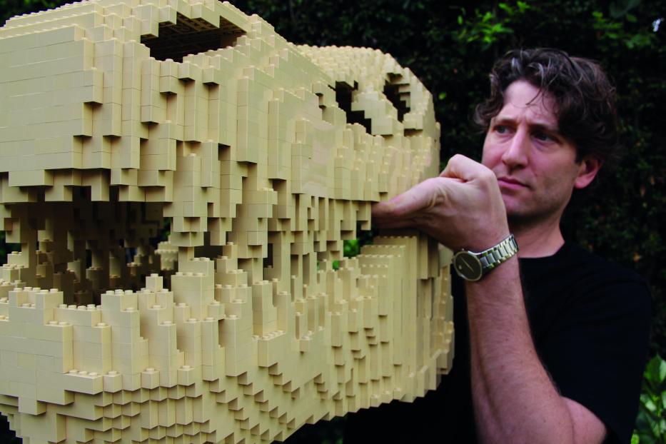 Ein Mann berührt einen Dinosaurierschädel, der aus hellbeigen Legosteinen gebaut wurde.