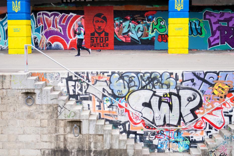 Eine Person joggt vor einer Wand mit Graffiti und einem Anti-Putin-Porträt.