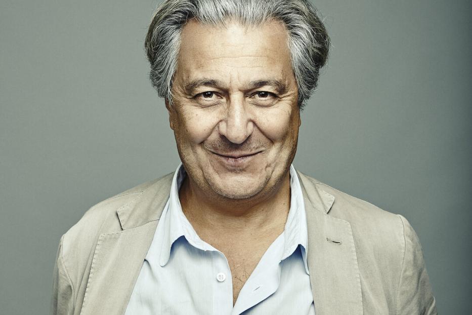 Ein lächelnder Mann mit grauem Haar trägt ein helles Sakko und ein hellblaues Hemd.