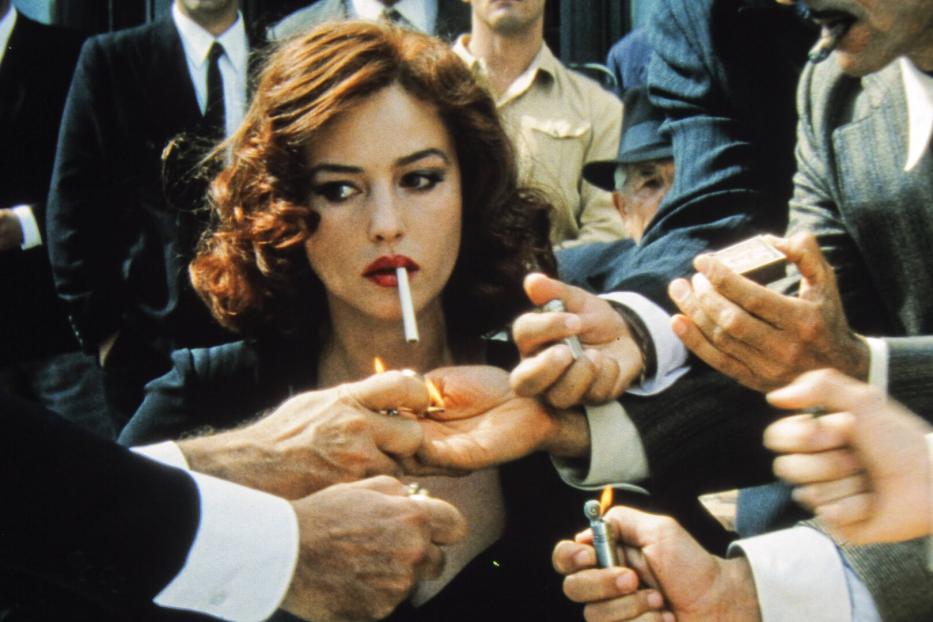 Monica Bellucci mit Zigarette im Mund, umringt von Männern, die ihr Feuer geben.
